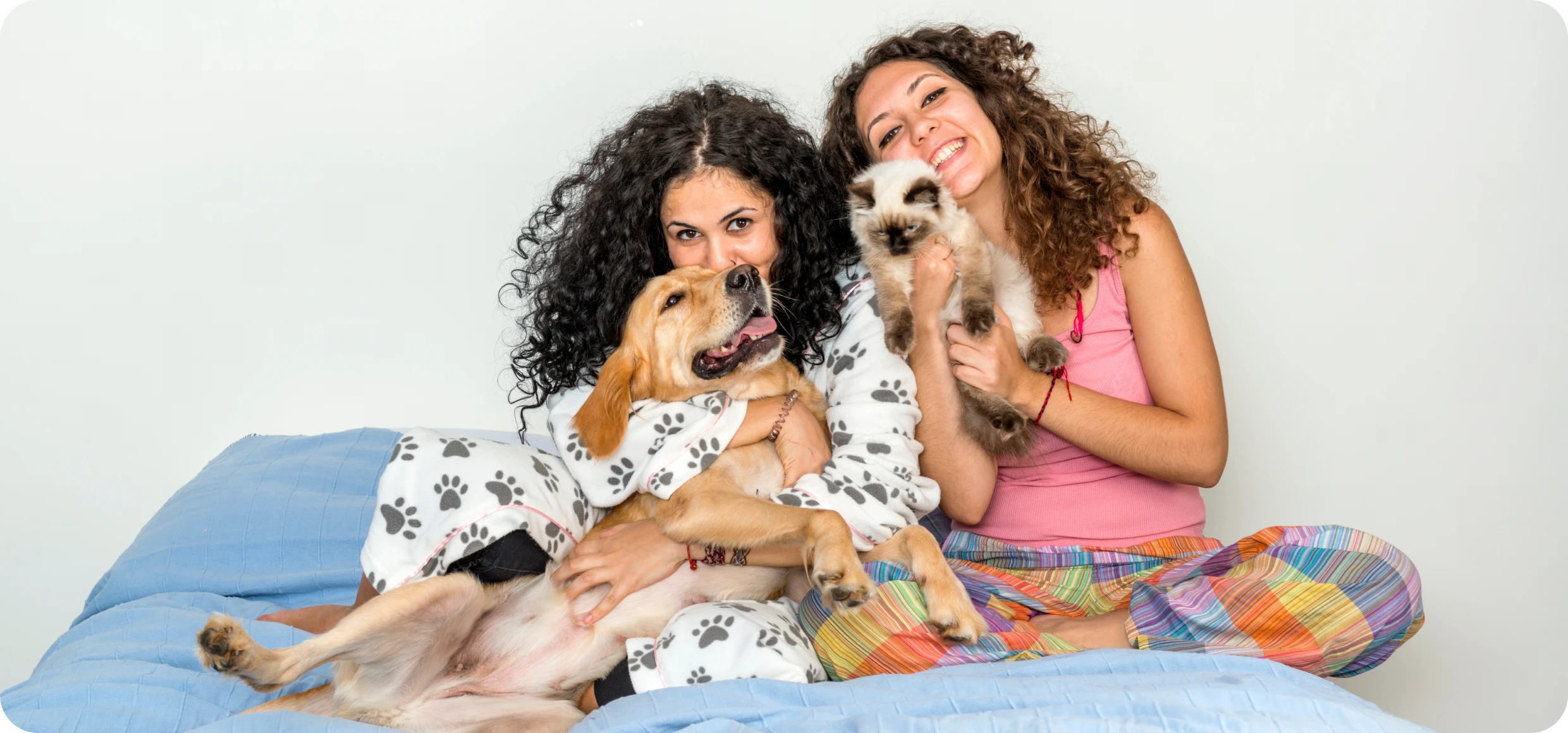 Two young women in pajamas cuddling a golden retriever and a cat.